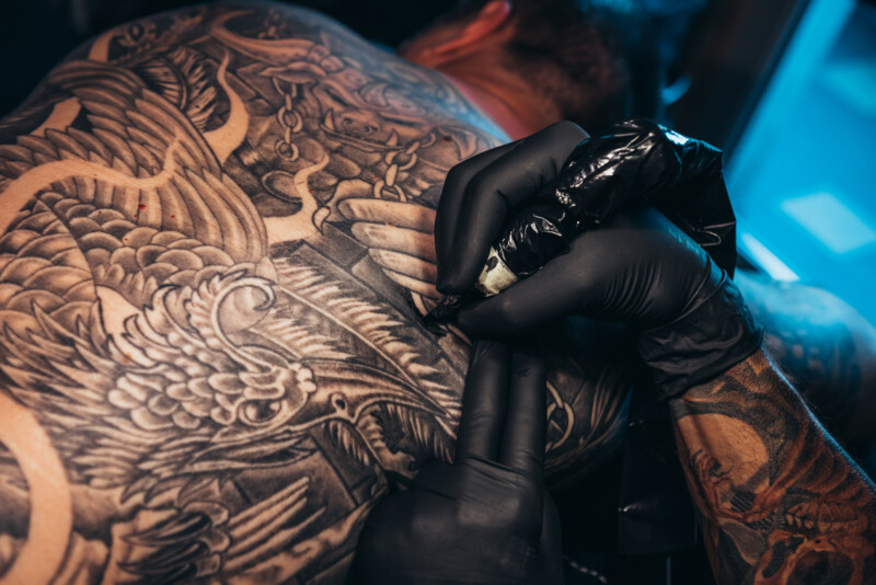 Cropped shot of a tattooed man back and an artist hands holding a tattoo machine