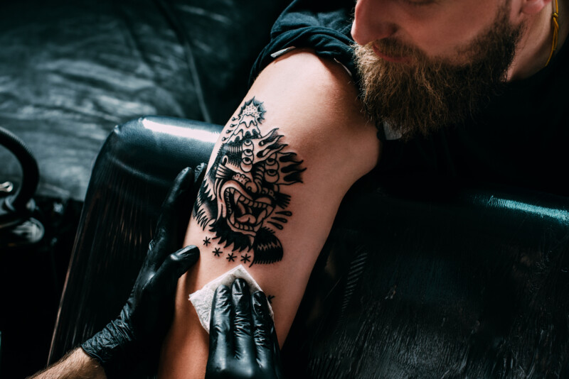 cropped shot of tattoo artist in gloves working on tattoo on shoulder in salon